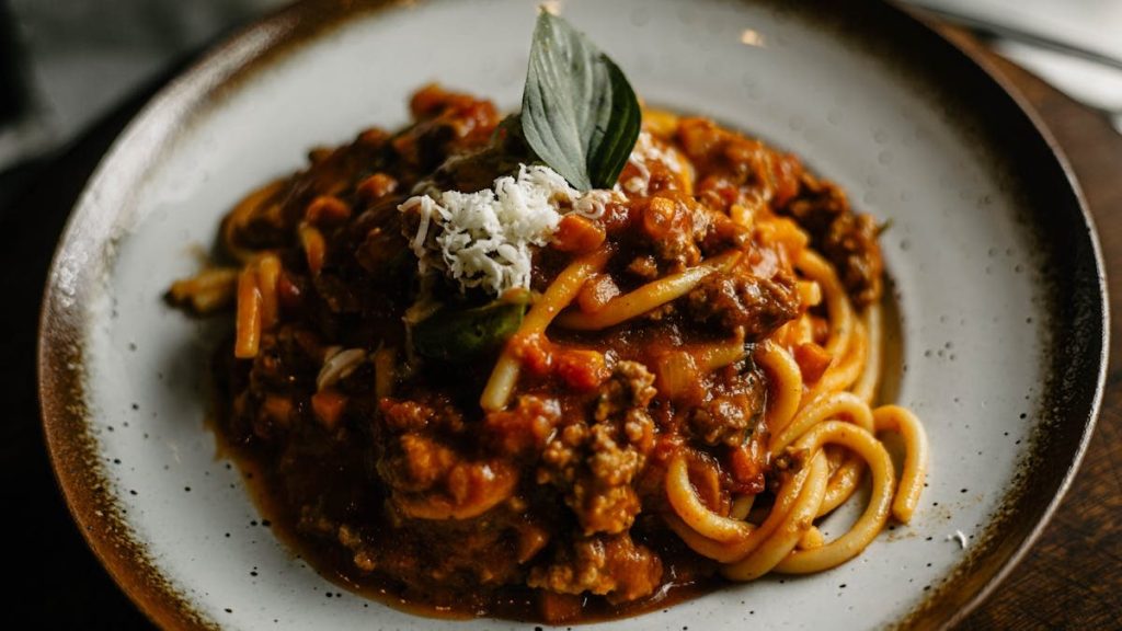 A close-up of flavorful Italian pasta with rich meat sauce garnished with basil and cheese.